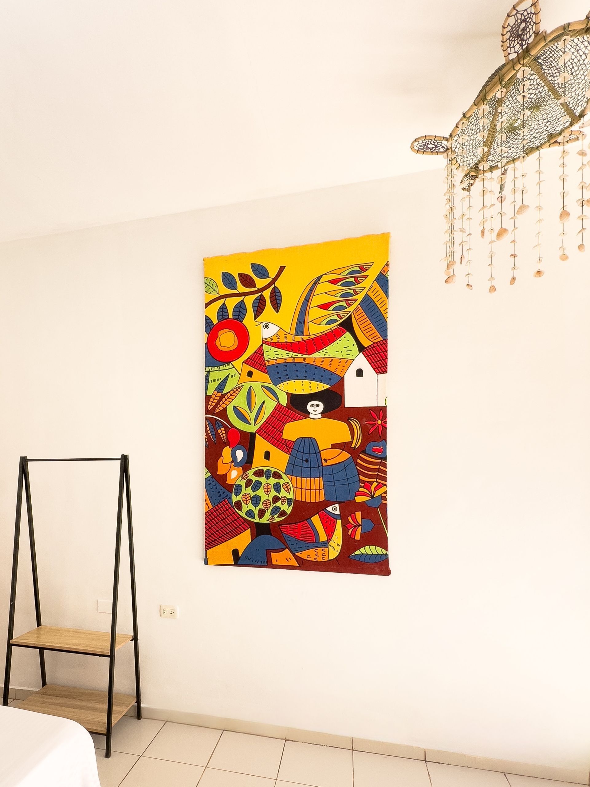 Obra de arte abstracta colorida sobre una pared blanca, cerca de un perchero y un candelabro ornamentado.