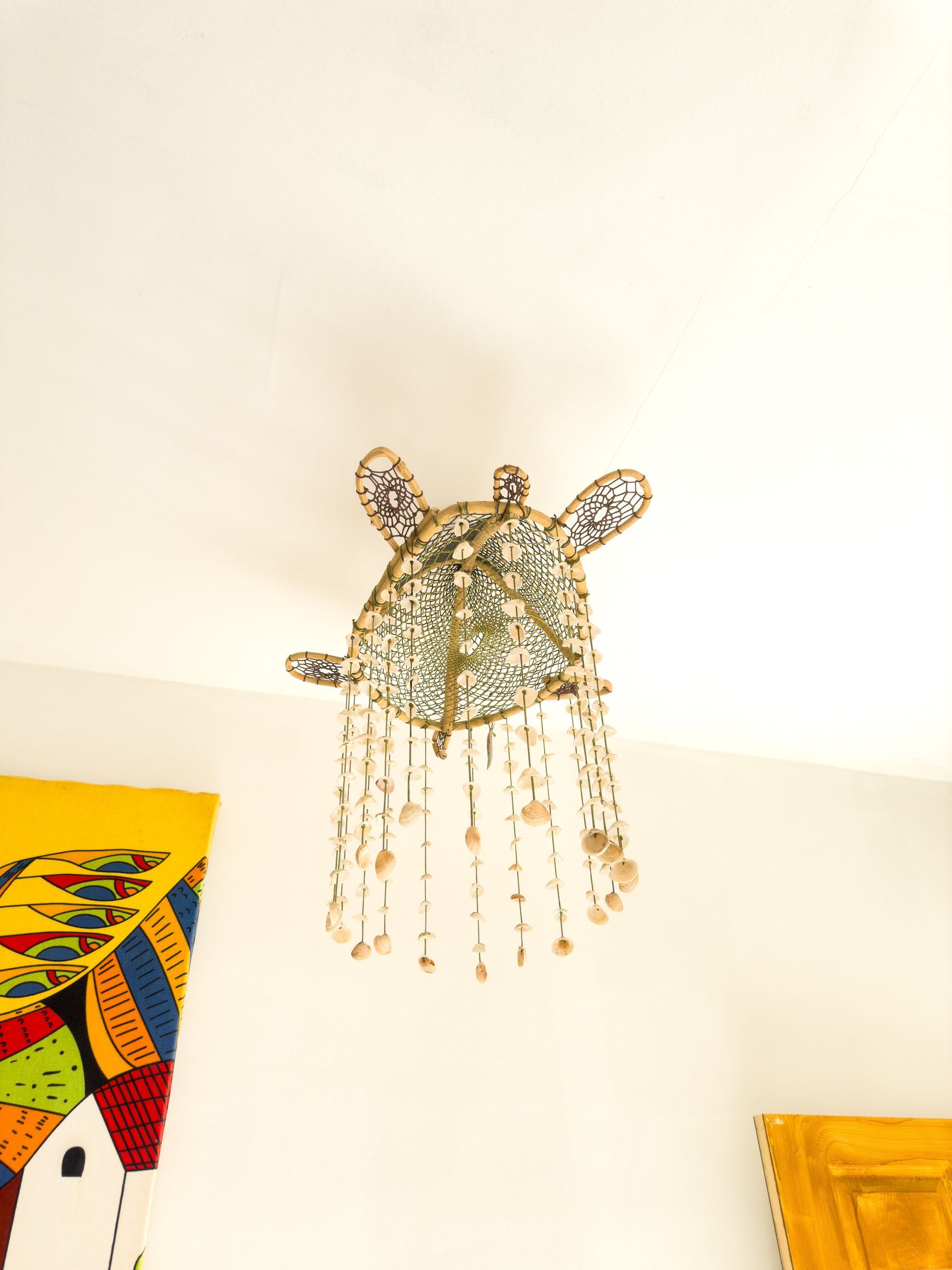 Lámpara de techo con forma de jirafa y cuentas colgantes, situada sobre un techo blanco con arte de pared colorido.