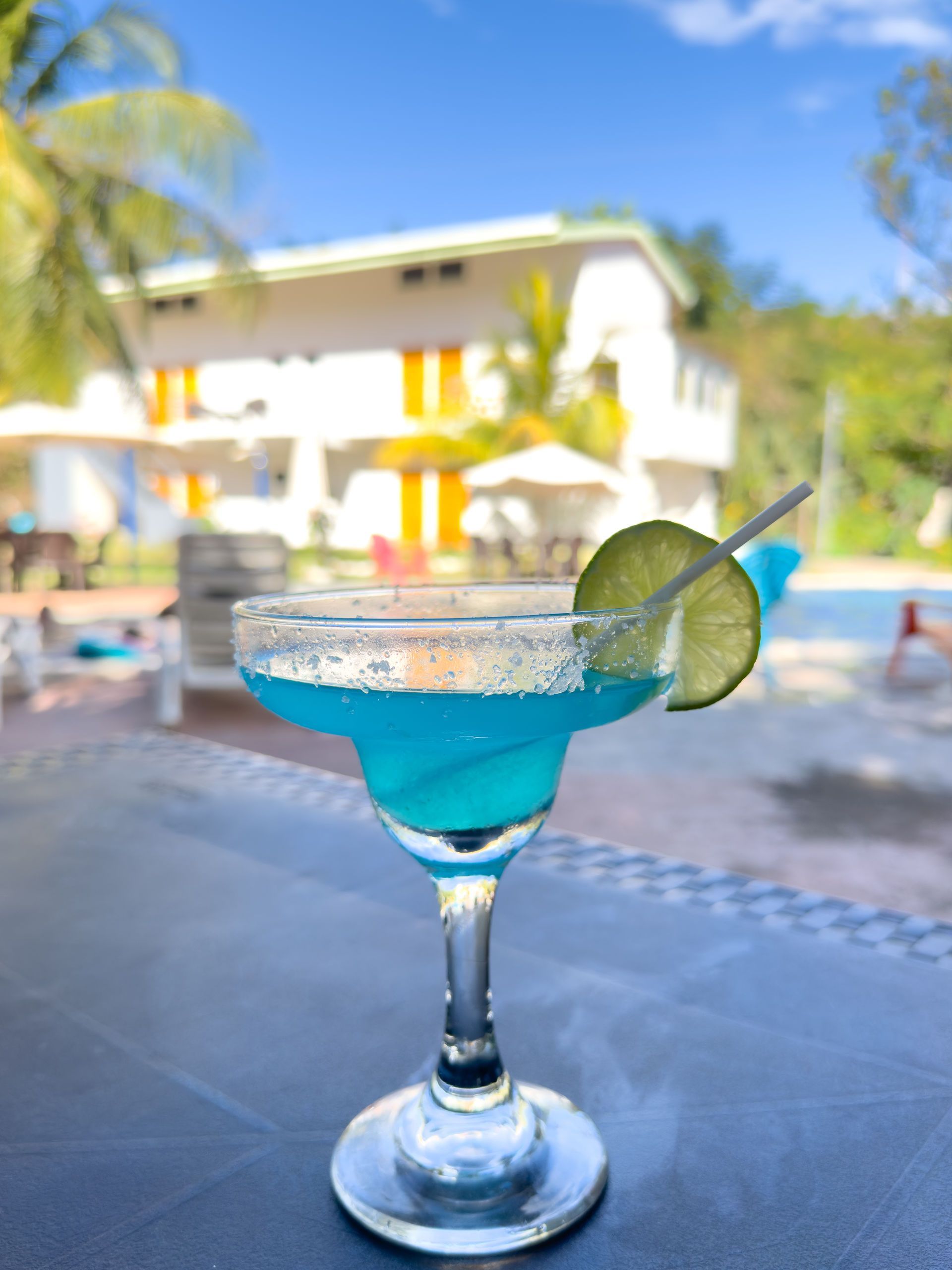 Margarita azul con rodaja de lima, colocada sobre una mesa en un resort tropical.