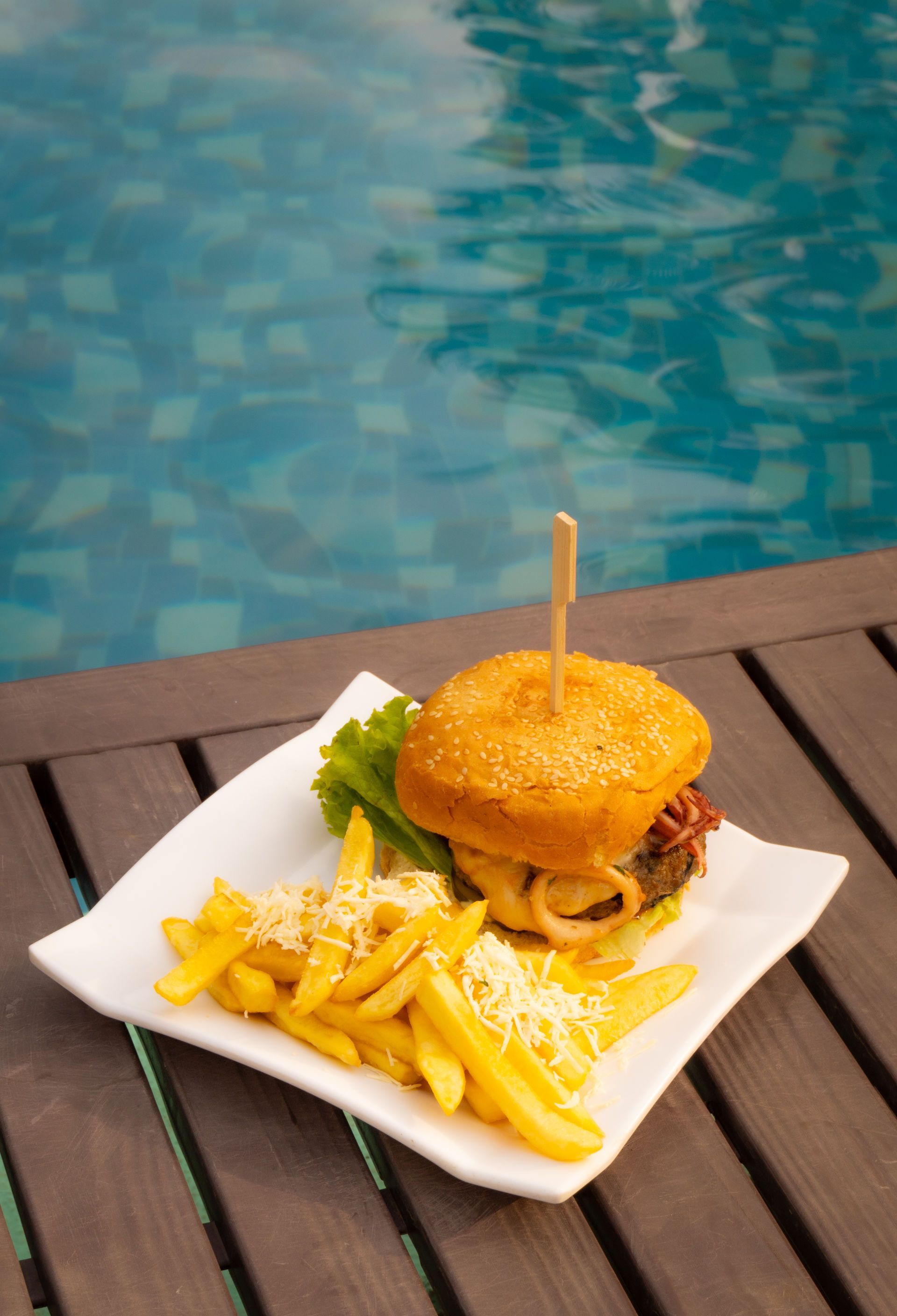 Hamburguesa y patatas fritas en un plato junto a una piscina