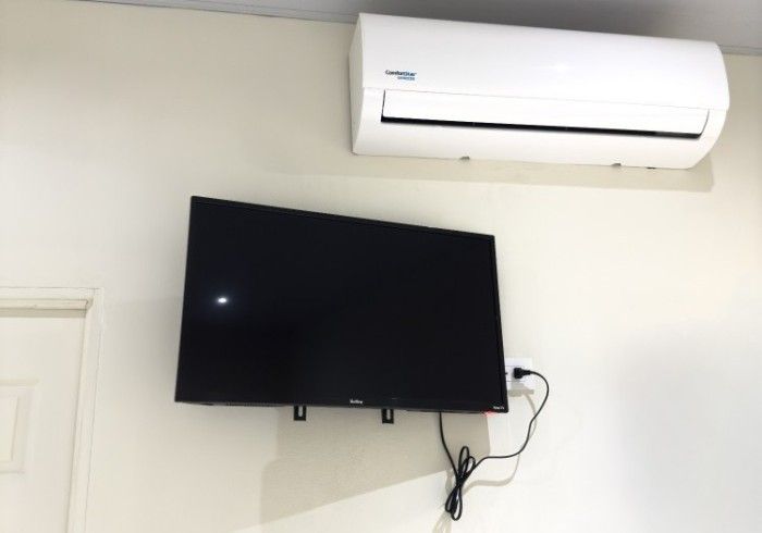 Aire acondicionado encima de un televisor montado en la pared, en una pared blanca.