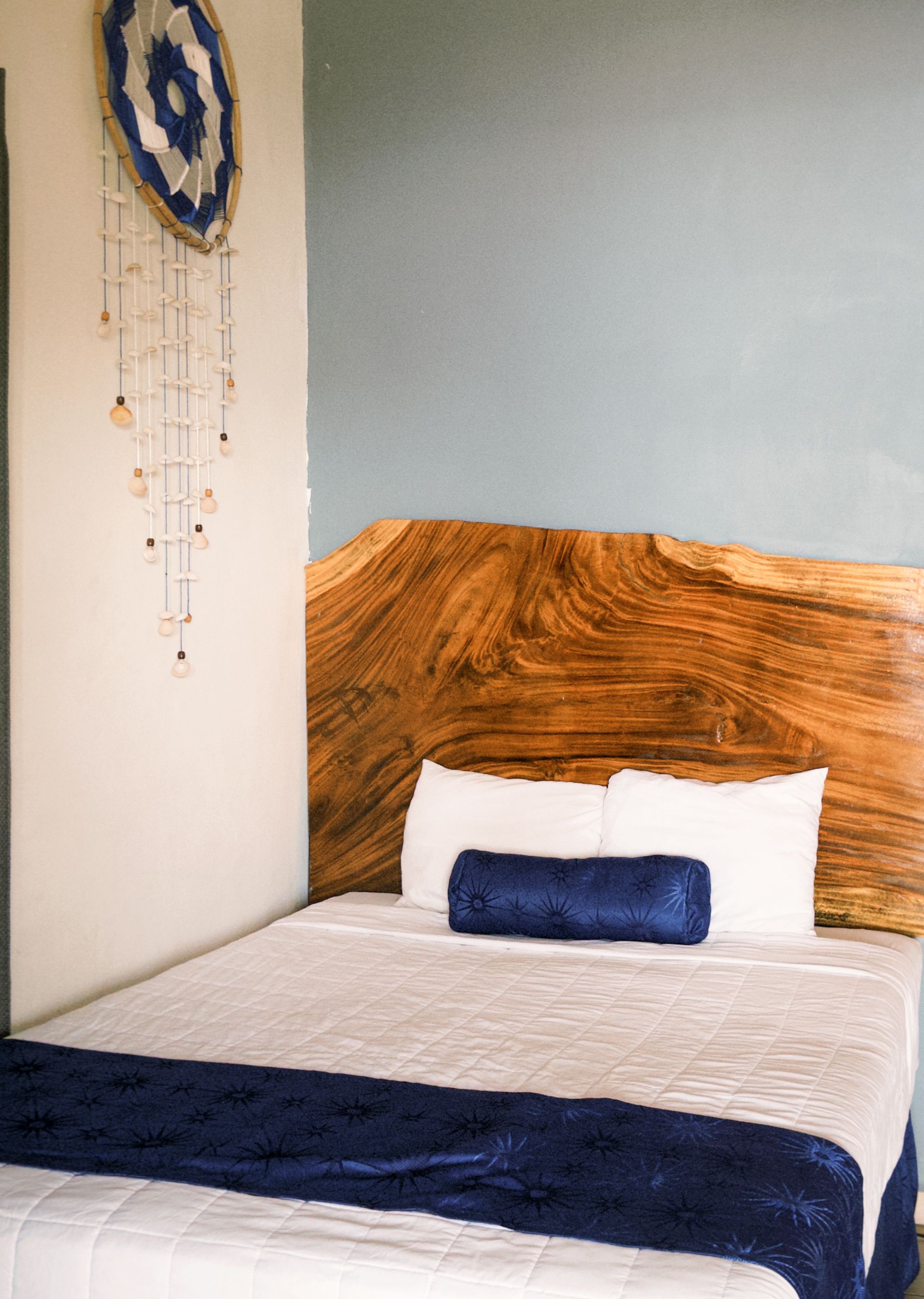Dormitorio con cabecero grande de madera, detalles en azul y atrapasueños.