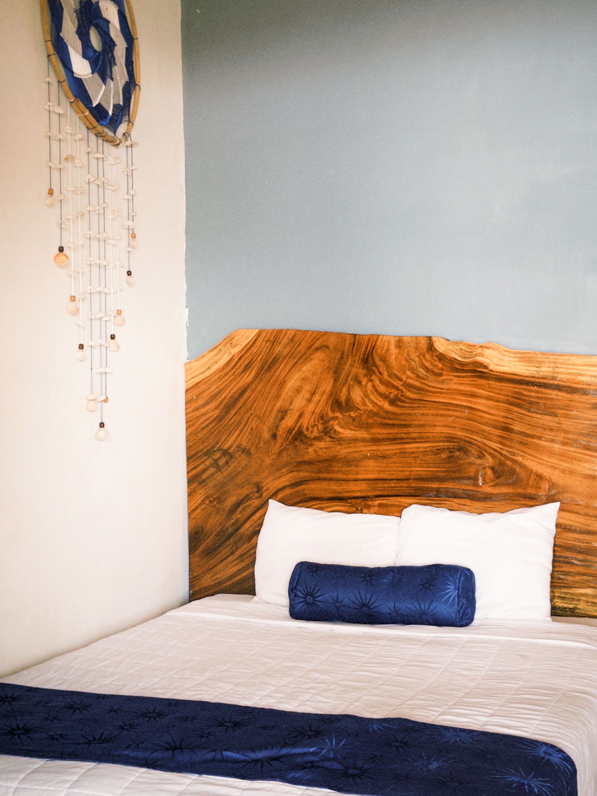 Cabecero de madera con almohadas blancas y detalles azules en un rincón del dormitorio.