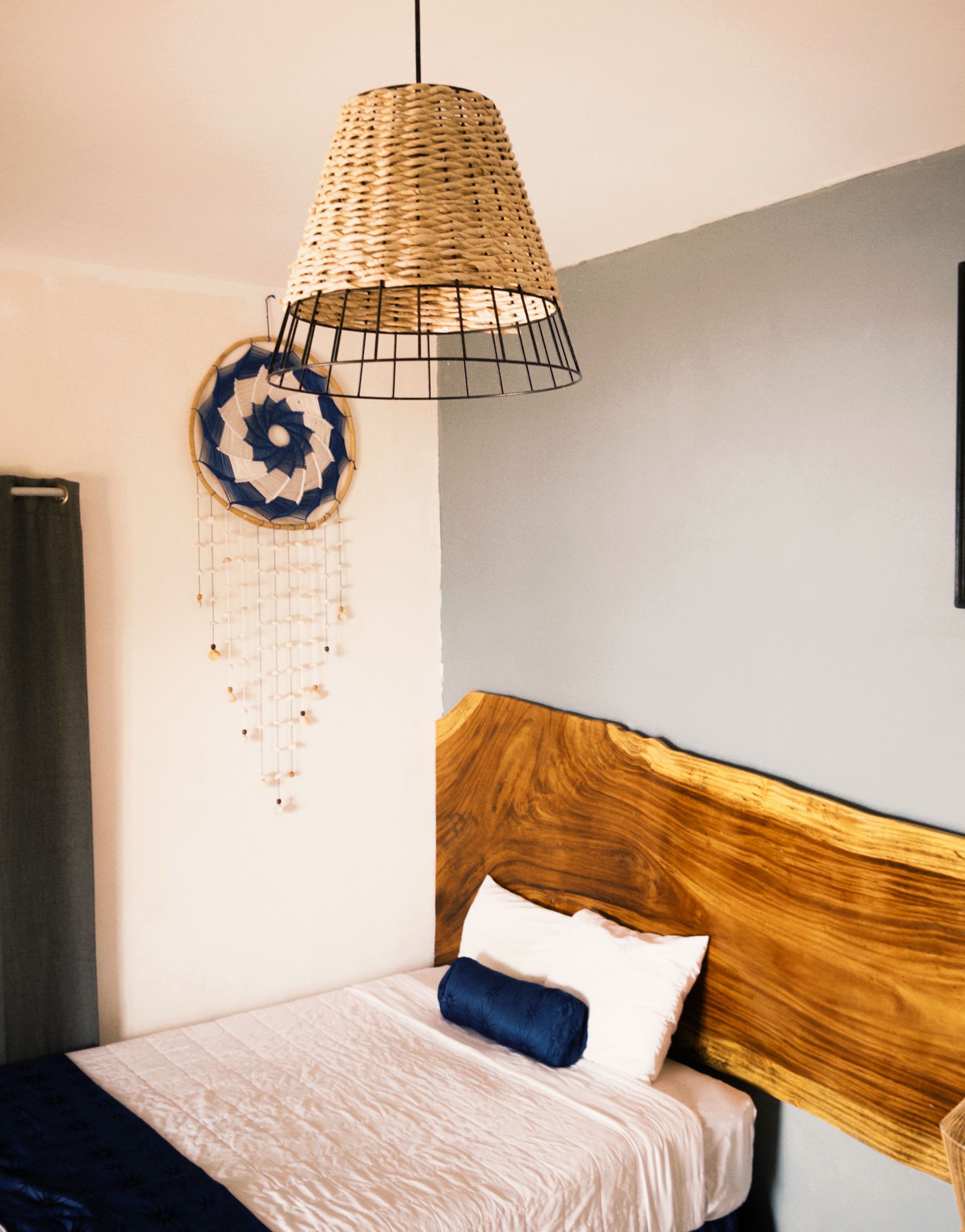 Dormitorio con cama individual, cabecero de madera, pantalla tejida, atrapasueños y ropa de cama azul y blanca.