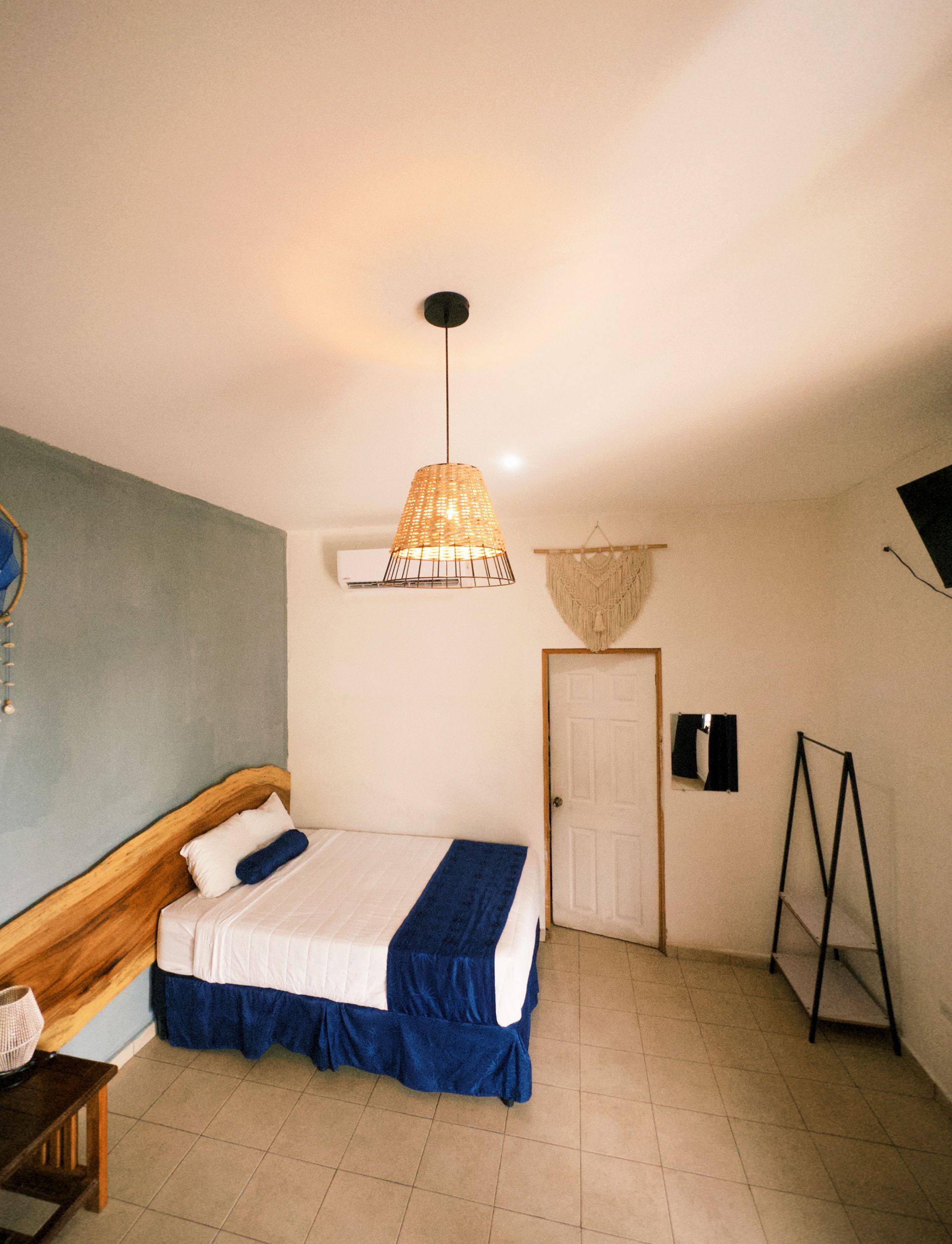 Dormitorio con cama, ropa de cama azul, lámpara tejida, cabecero de madera y puerta.