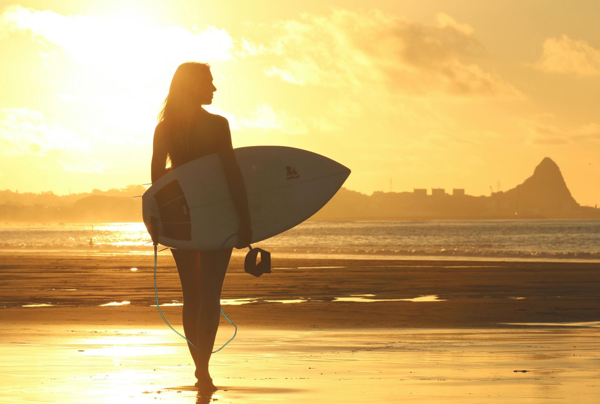 Mujer con tabla de surf caminando por la playa al atardecer.