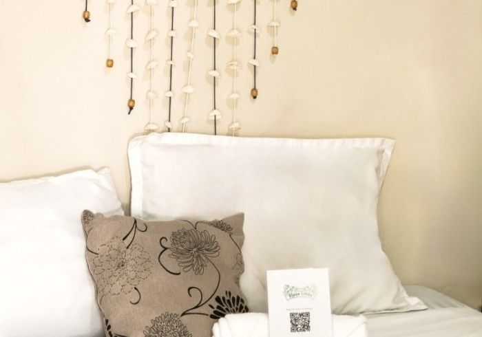 Cama con sábanas blancas, almohada floral, decoración de conchas, sobre pared beige.