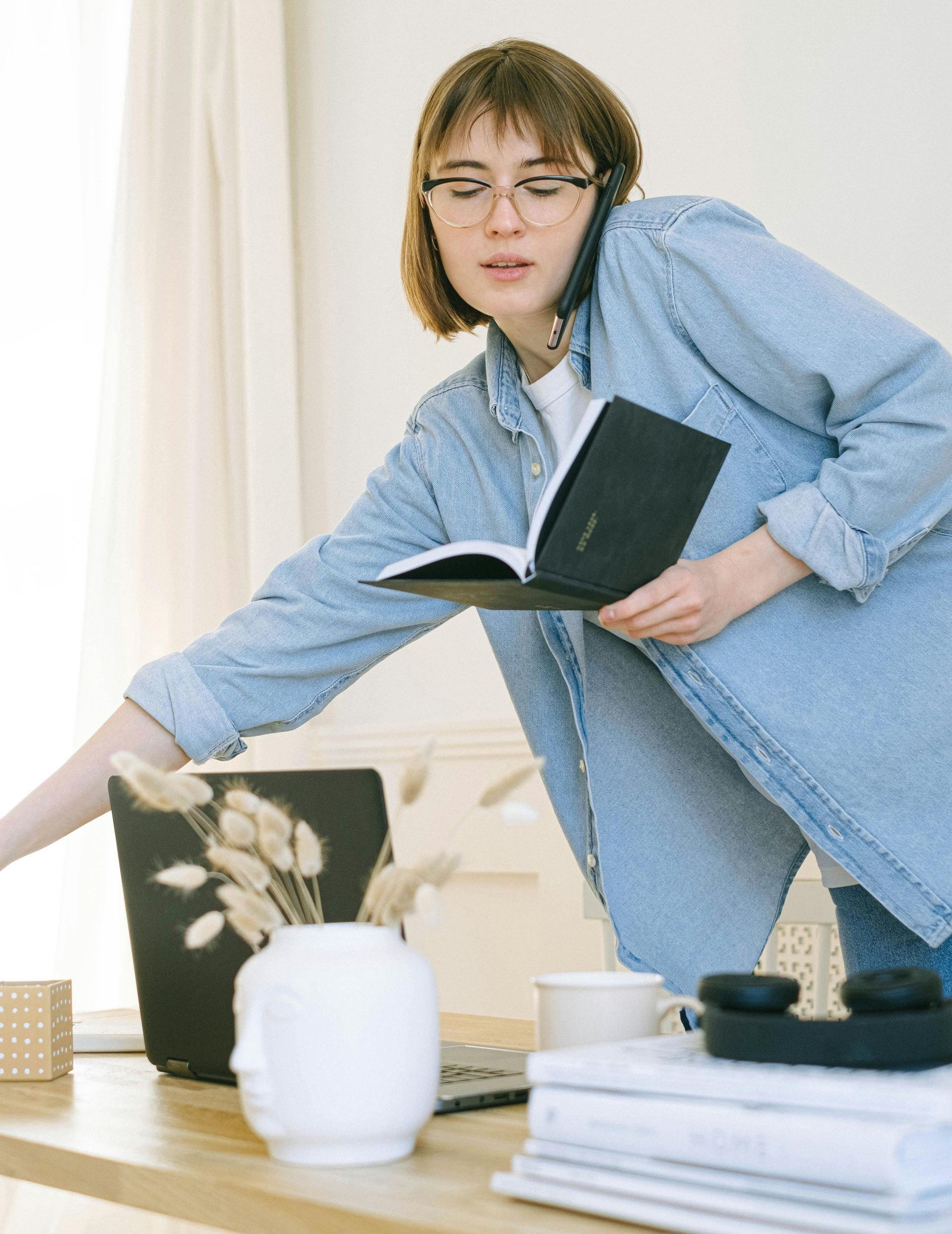 A woman is talking on a cell phone while holding a book.