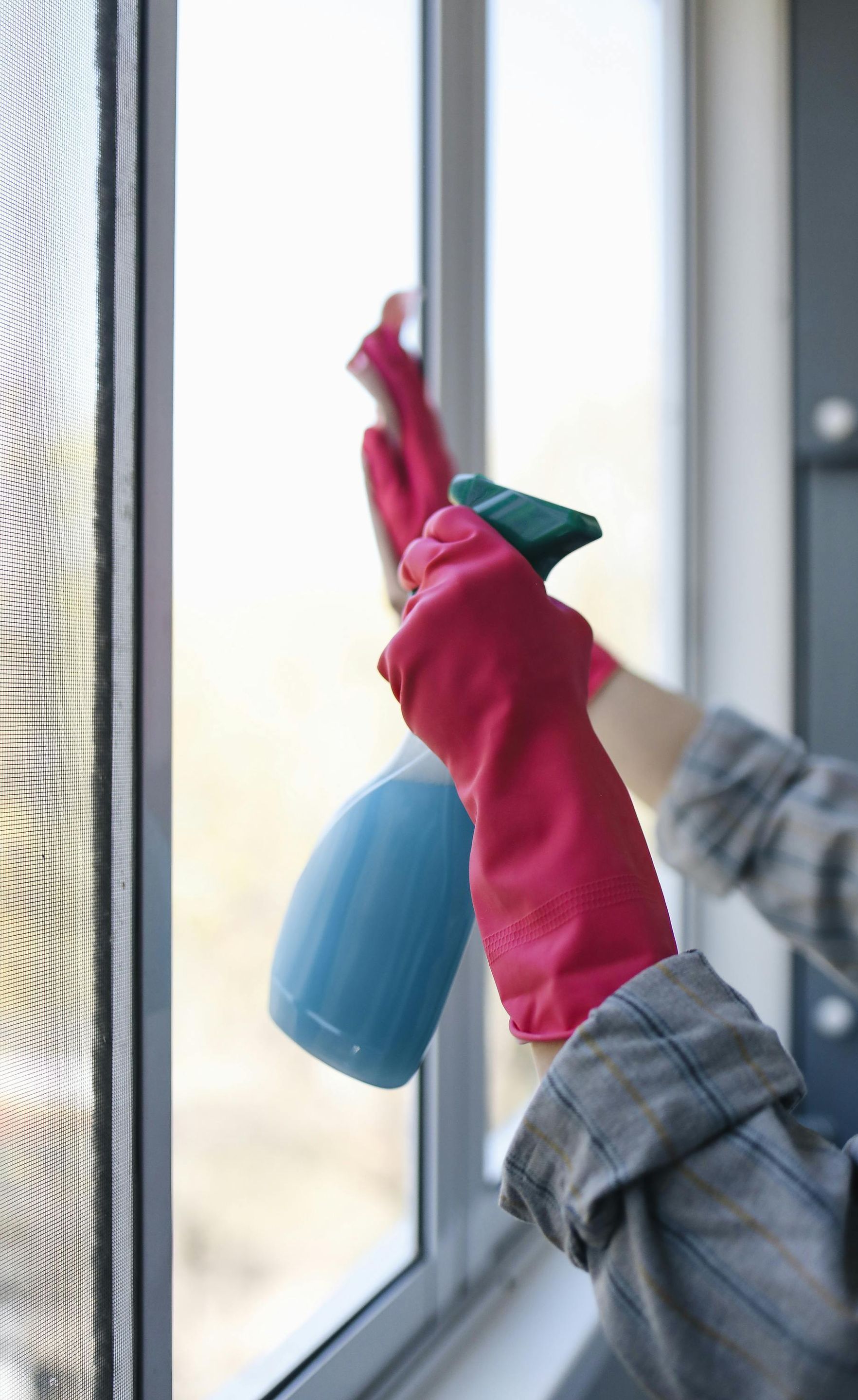 A person wearing red gloves is cleaning a window with a spray bottle.