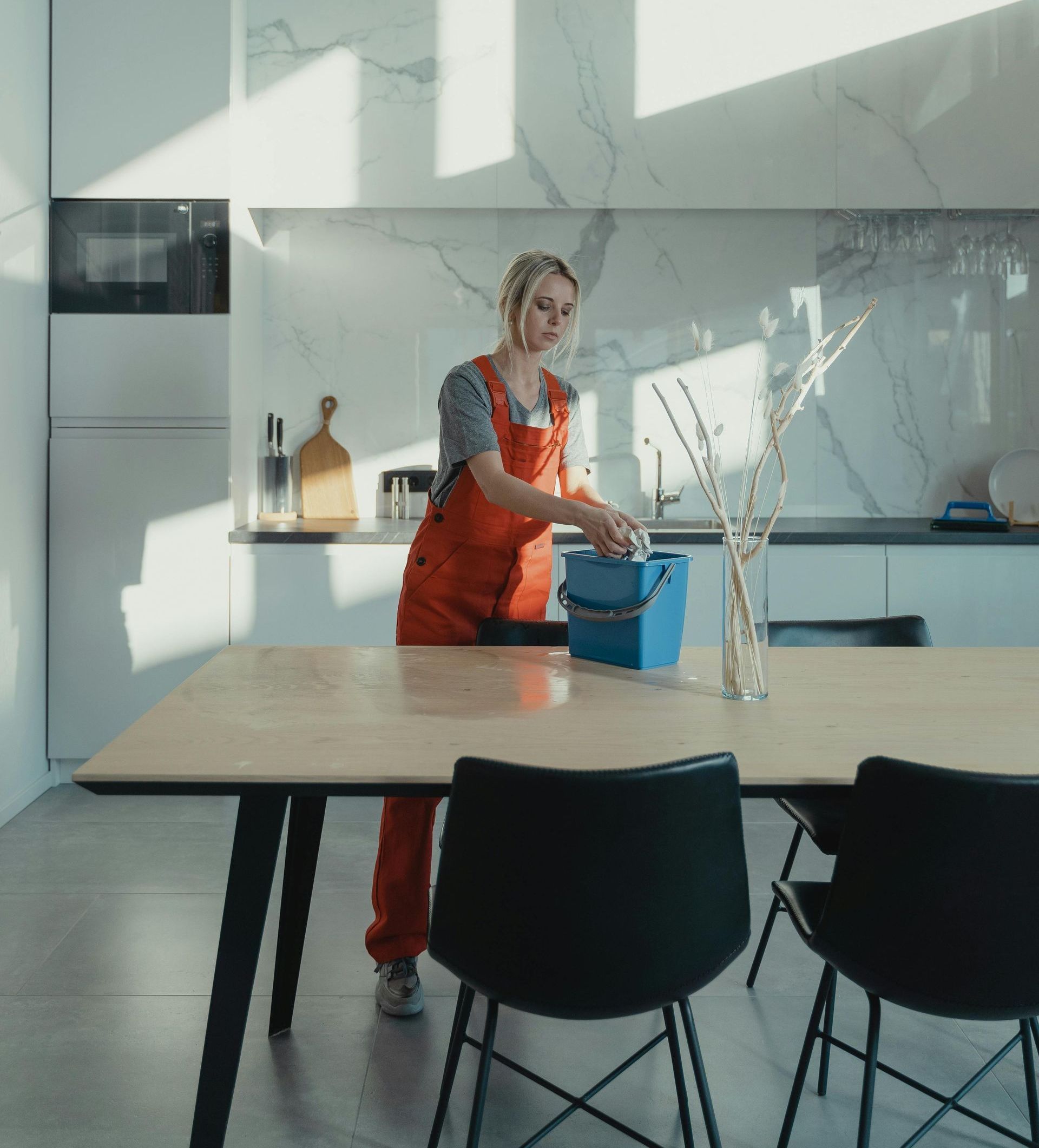 A woman in a red apron is cleaning a table with a blue bucket