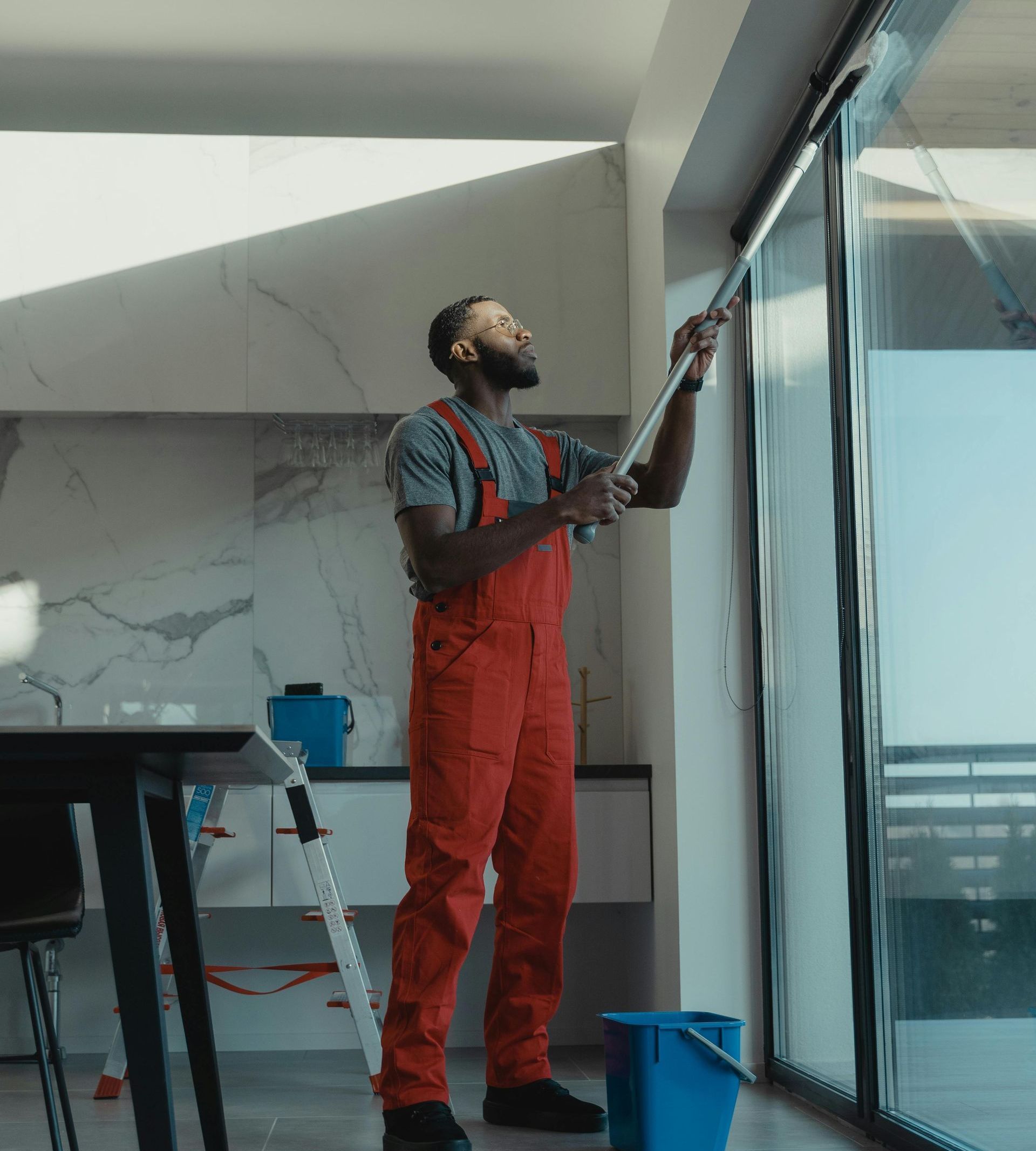 A man in red overalls is cleaning a window with a mop.