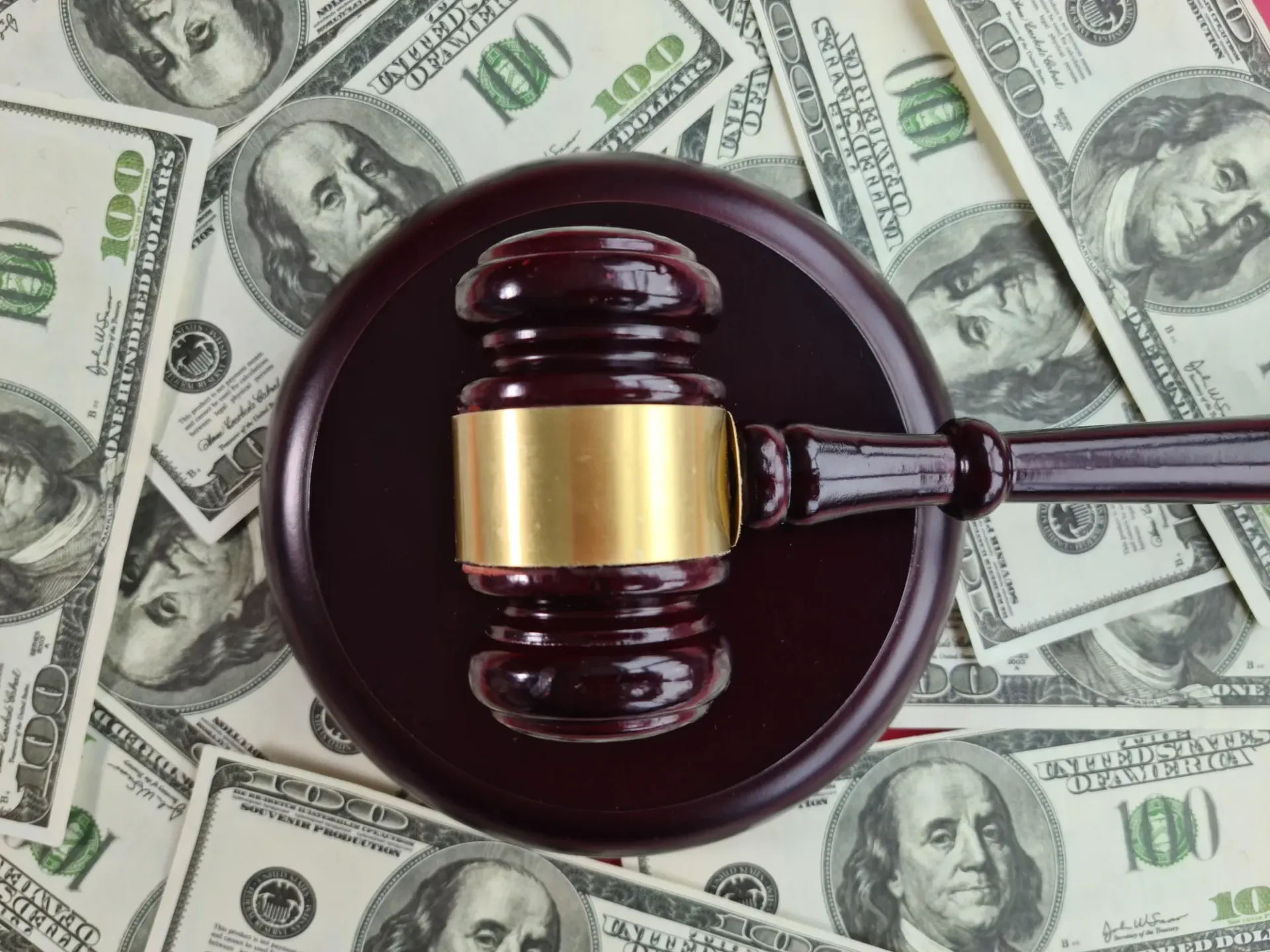 Gavel resting on a sound block, surrounded by scattered US $100 bills.