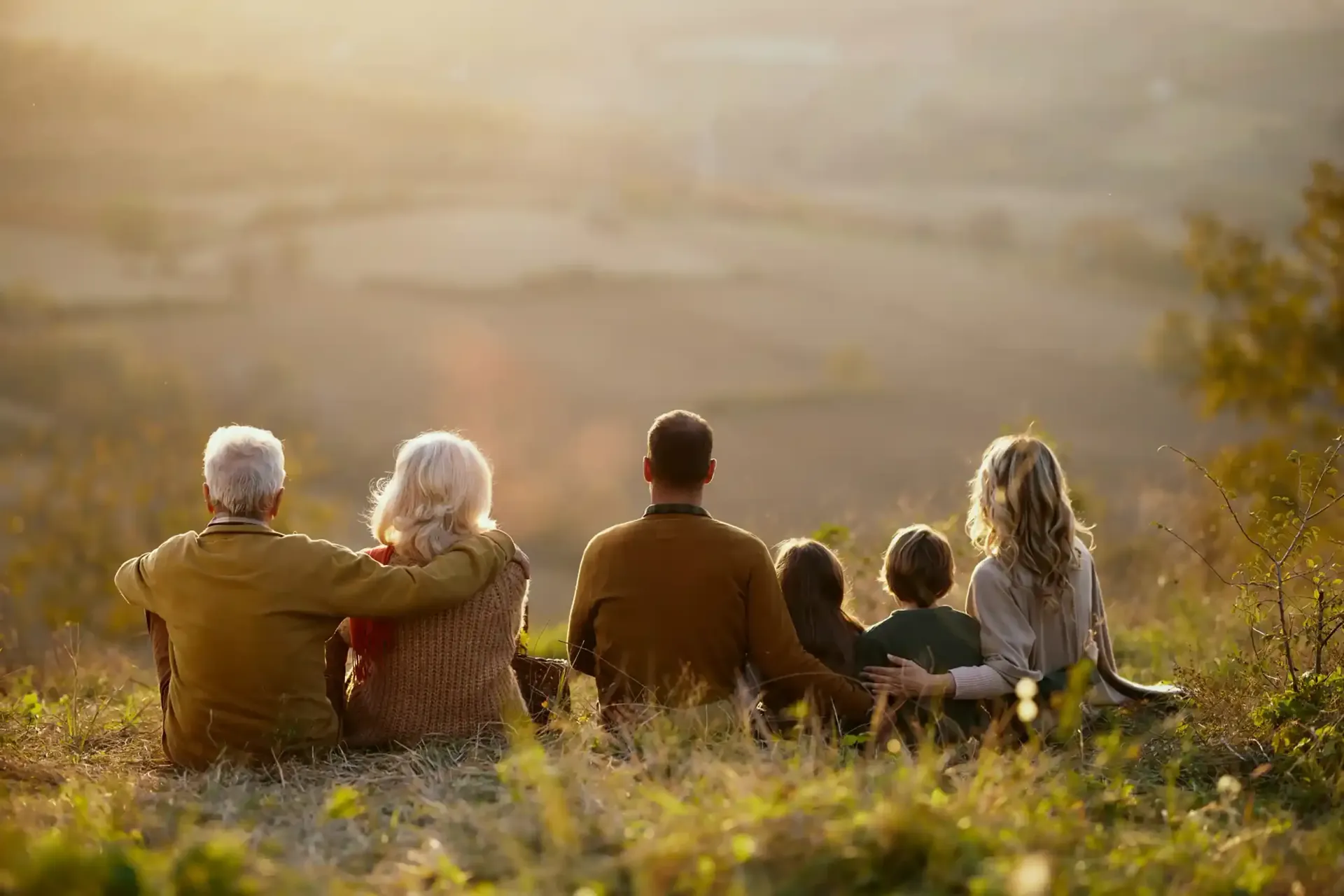 Family sitting on a hillside, overlooking a landscape, basking in the sunlight.