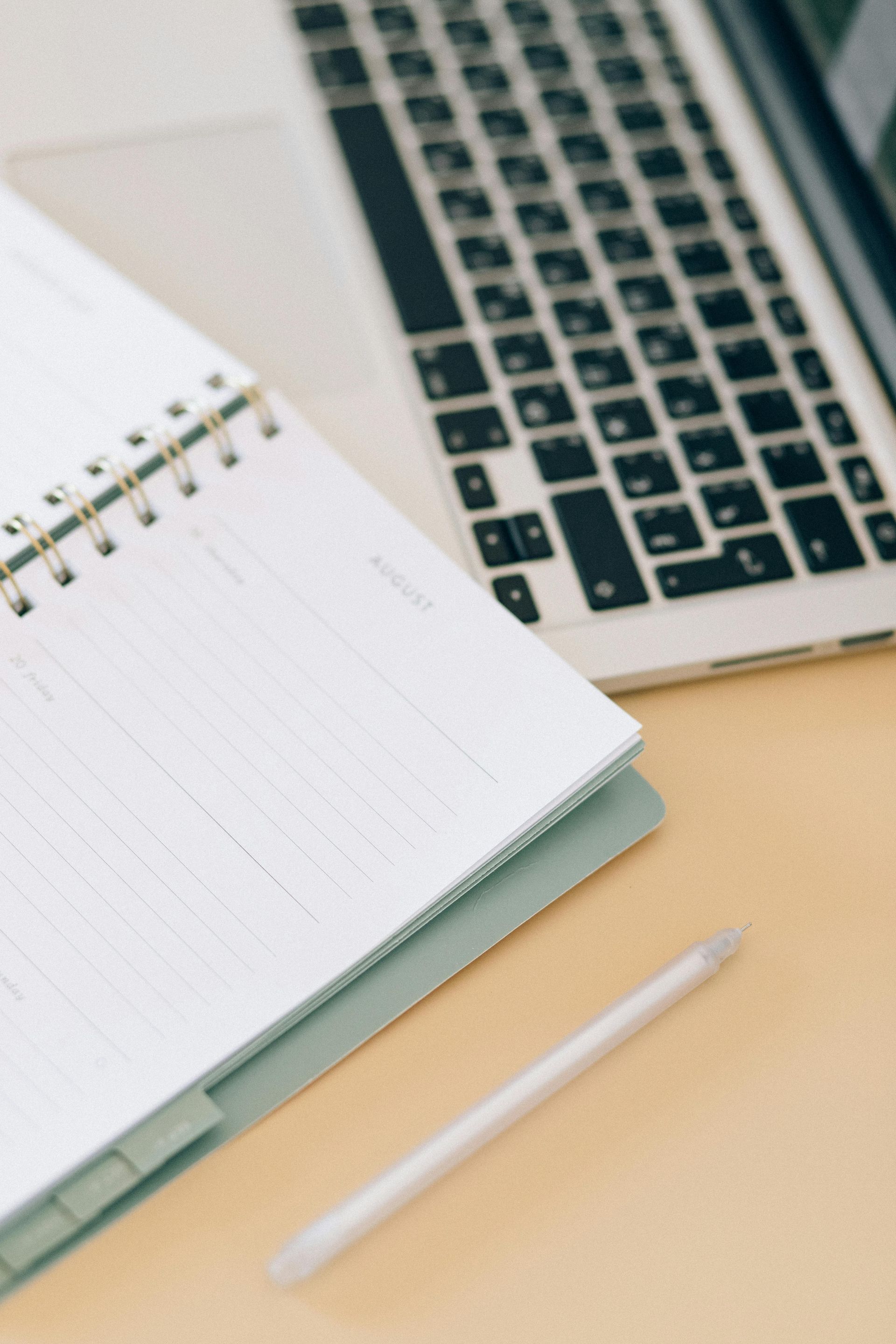 Notebook, pen, and laptop on a light-colored desk, ready for work or study.
