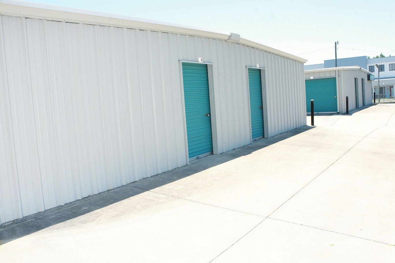 White metal storage units with turquoise doors along a concrete path under a bright sky.