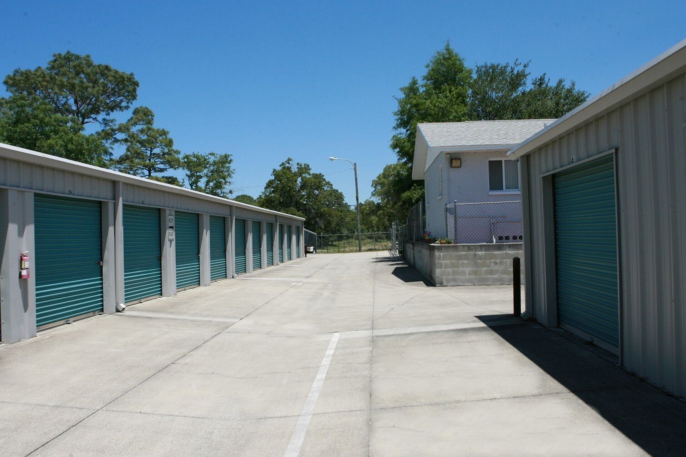 Storage units with teal doors under a bright blue sky. Concrete drive.
