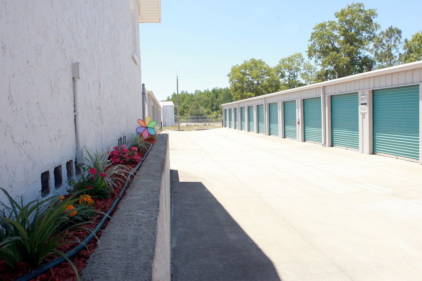 Exterior view of a storage facility with teal doors and a concrete walkway on a sunny day.