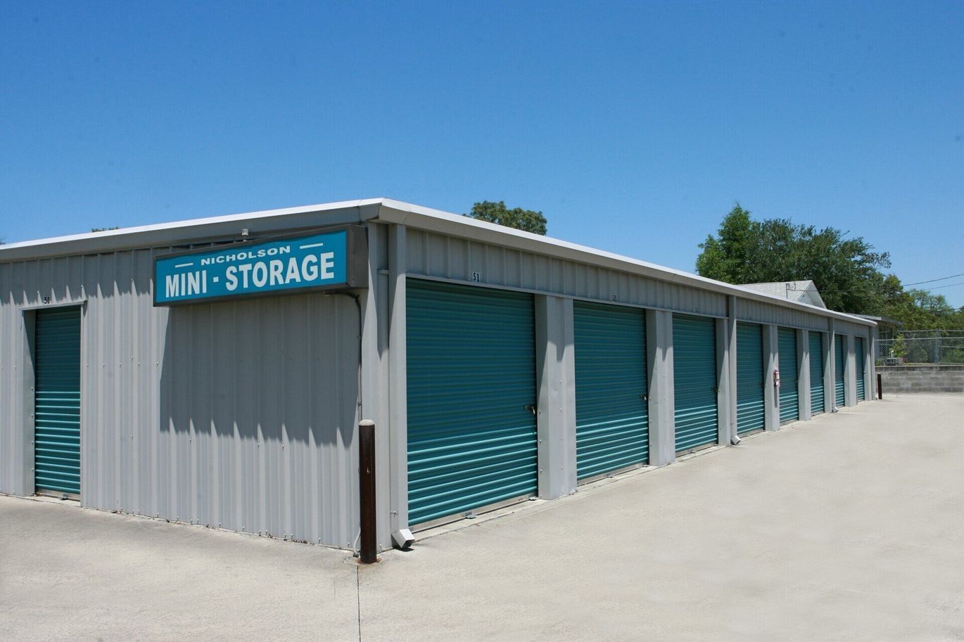 Mini storage units with teal doors under a blue sky.