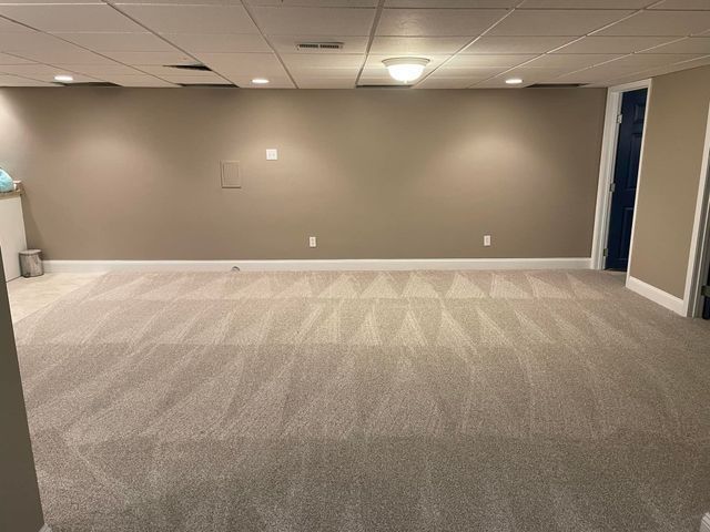 An empty basement with a carpeted floor and tan walls.
