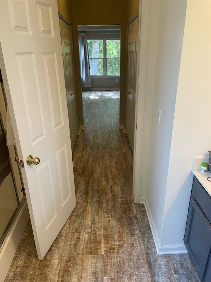 A hallway in a house with hardwood floors and a bathroom.