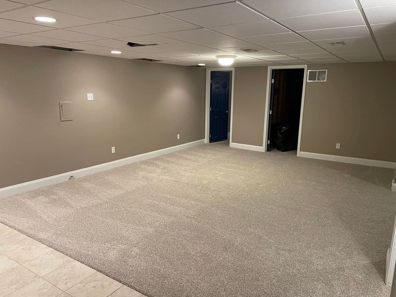 An empty basement with a carpeted floor and beige walls.