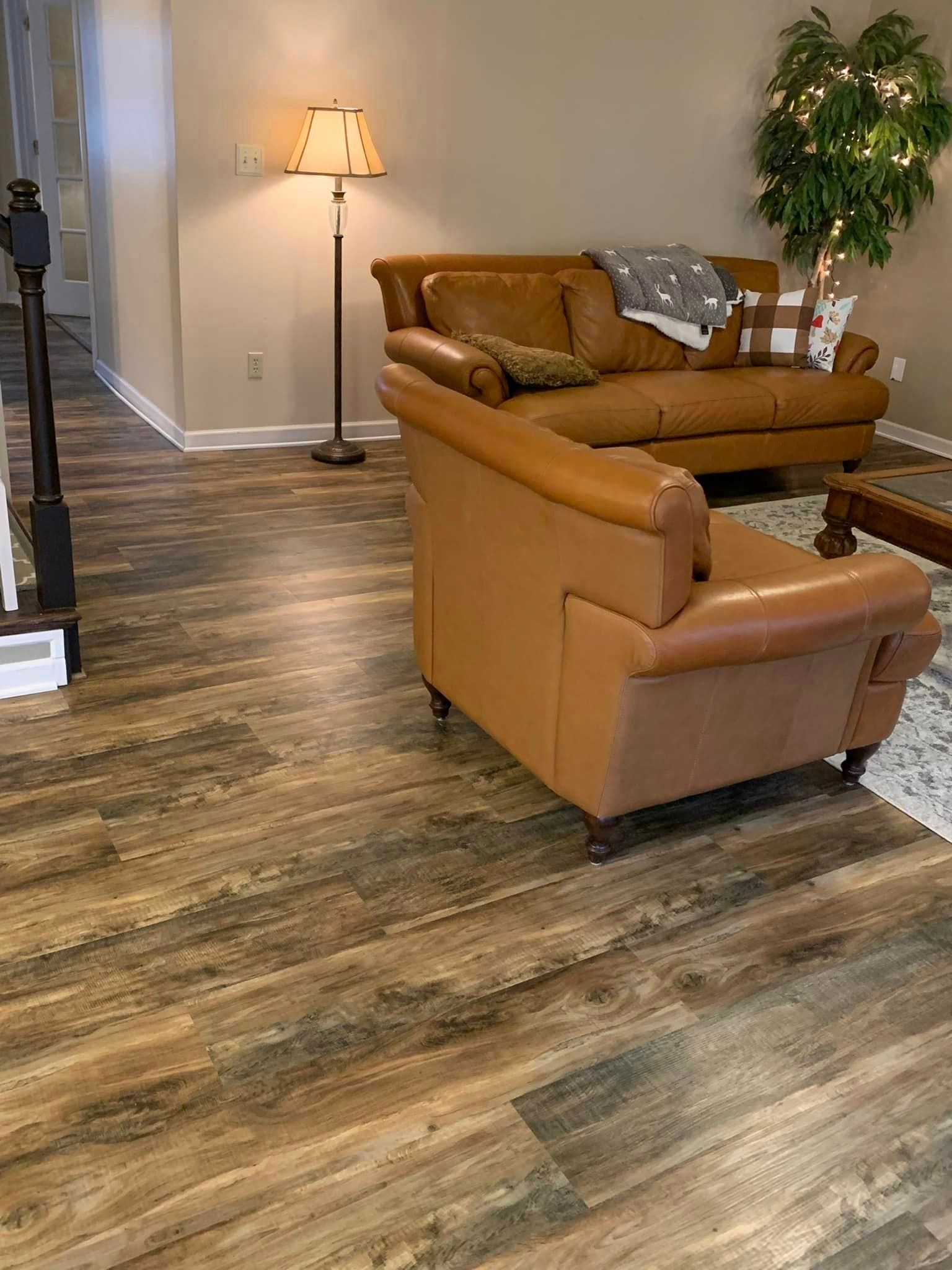A living room with hardwood floors , a couch , chair and lamp.