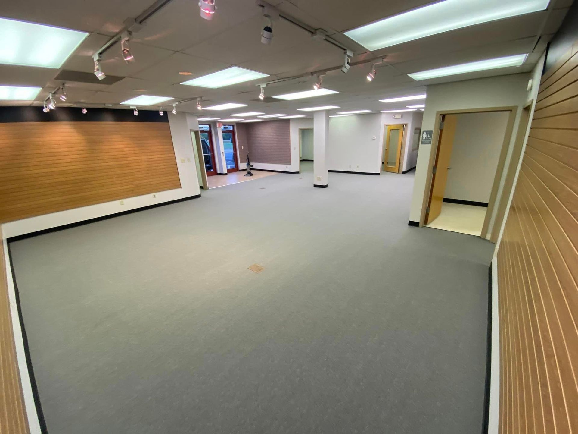 A large empty room with a carpeted floor and a wooden wall.