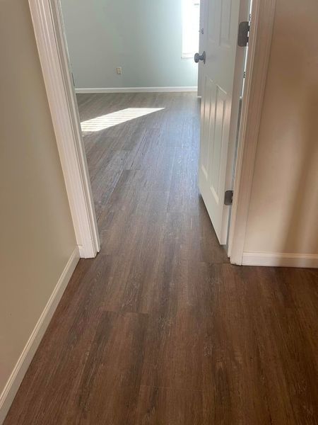 A hallway with hardwood floors and a white door leading to a bedroom.