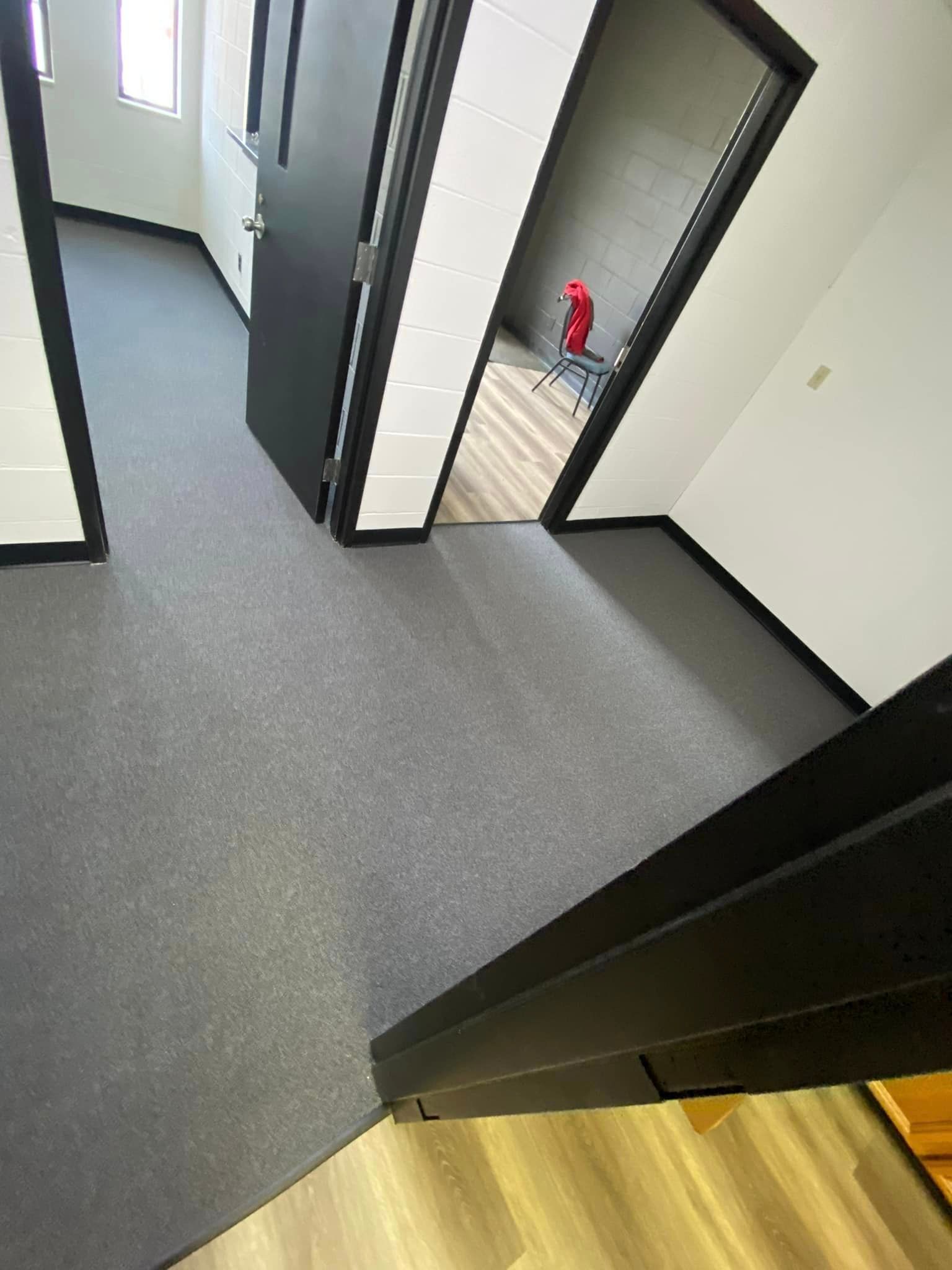 A hallway with a carpeted floor and a black door leading to a room.
