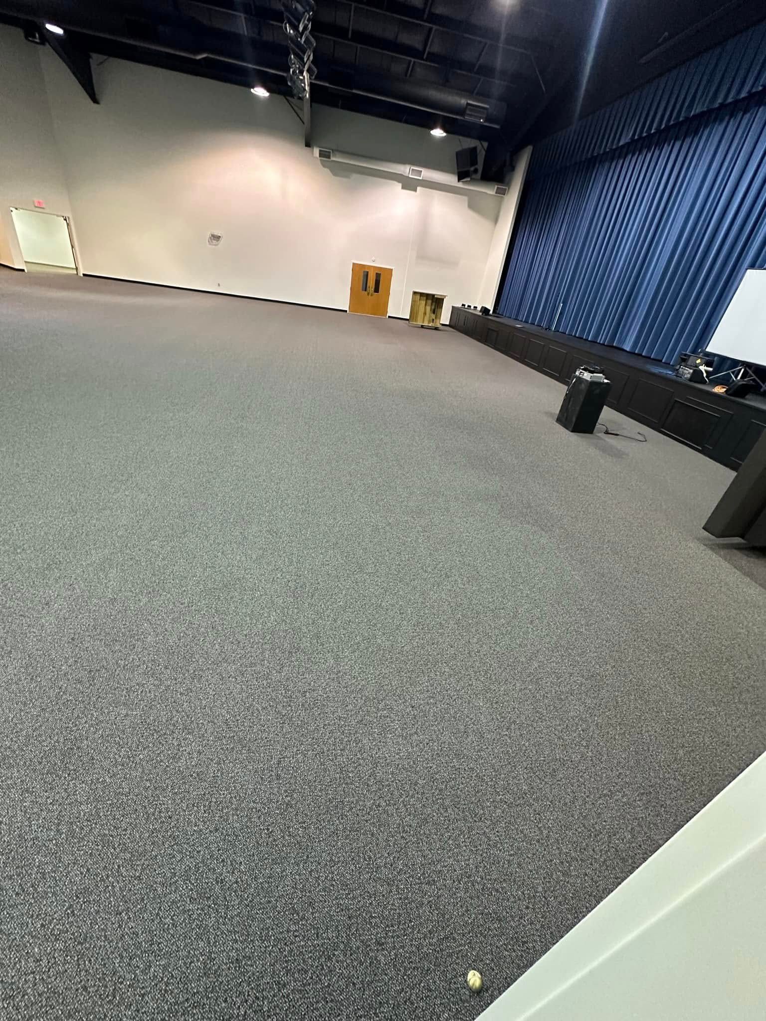 A large empty auditorium with a carpeted floor and a blue curtain.