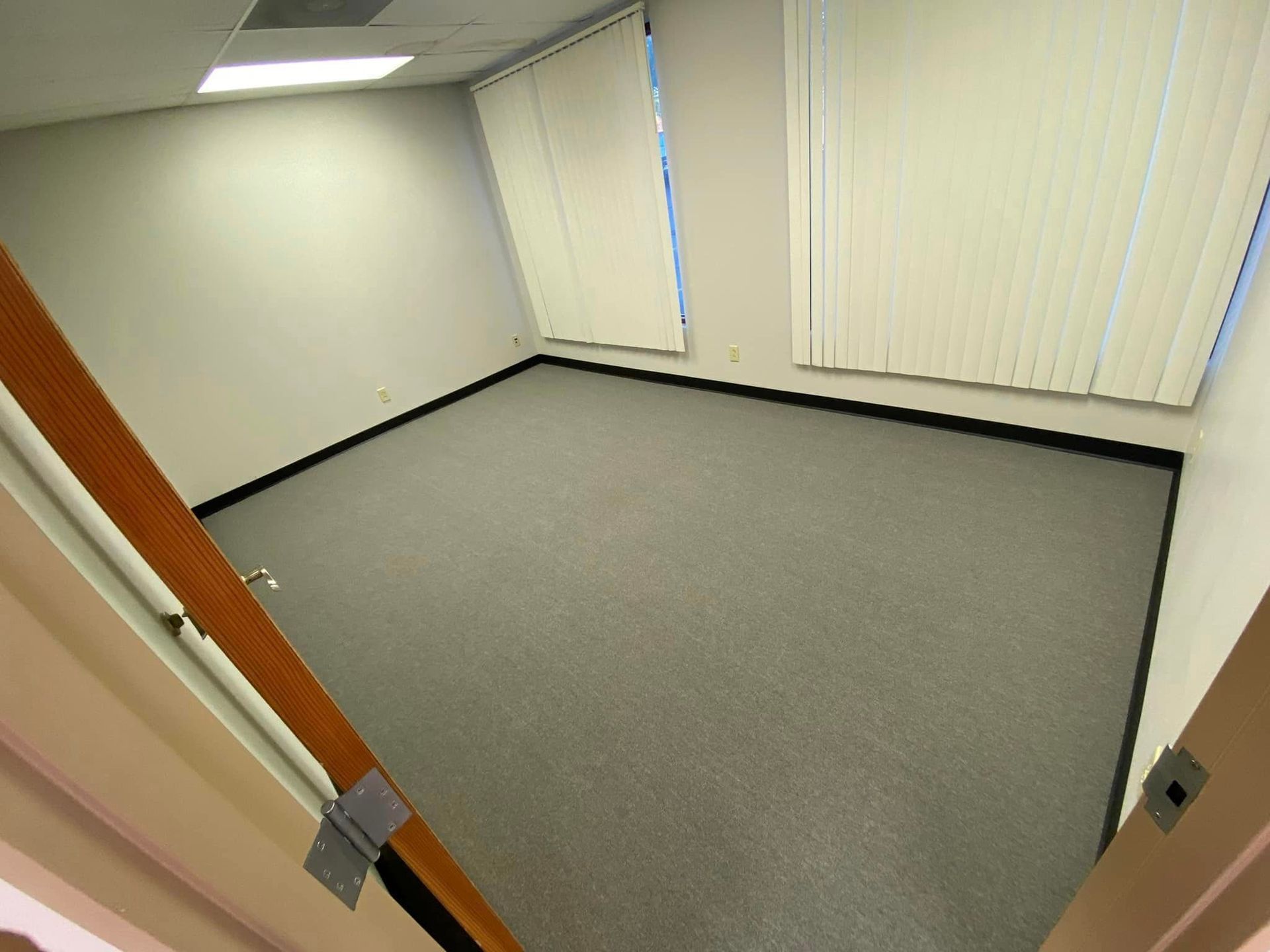 An empty room with a carpeted floor and blinds on the windows