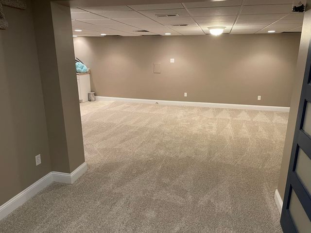 An empty basement with a carpeted floor and beige walls.
