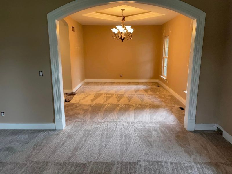 A dining room with a chandelier hanging from the ceiling and a carpeted floor.