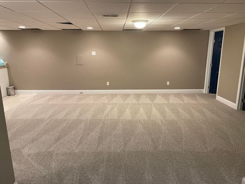 An empty basement with a carpeted floor and a ceiling.