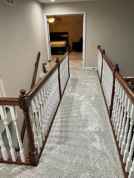 A hallway with stairs and a wooden railing leading to a bedroom.