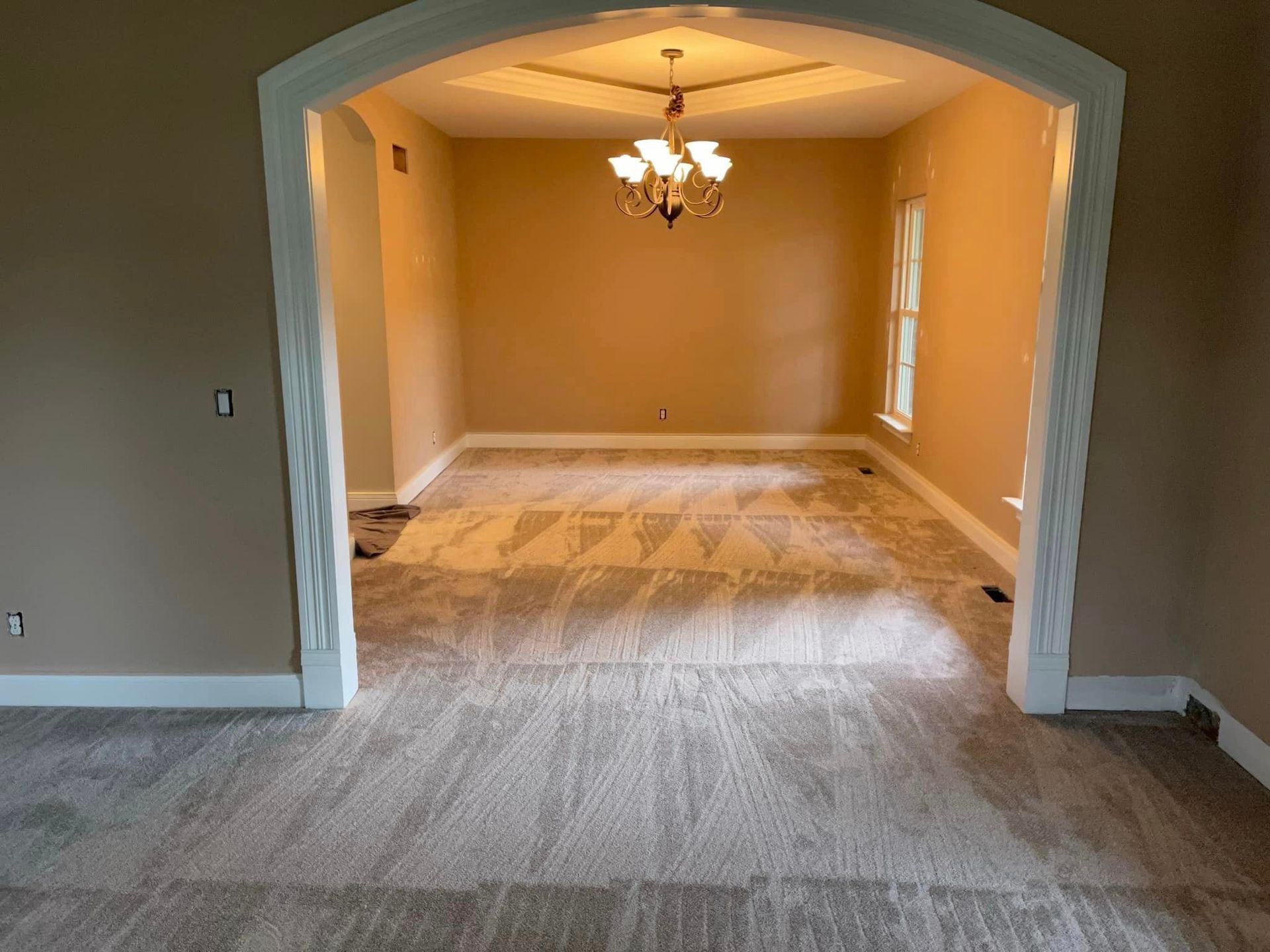 An empty dining room with a chandelier hanging from the ceiling.