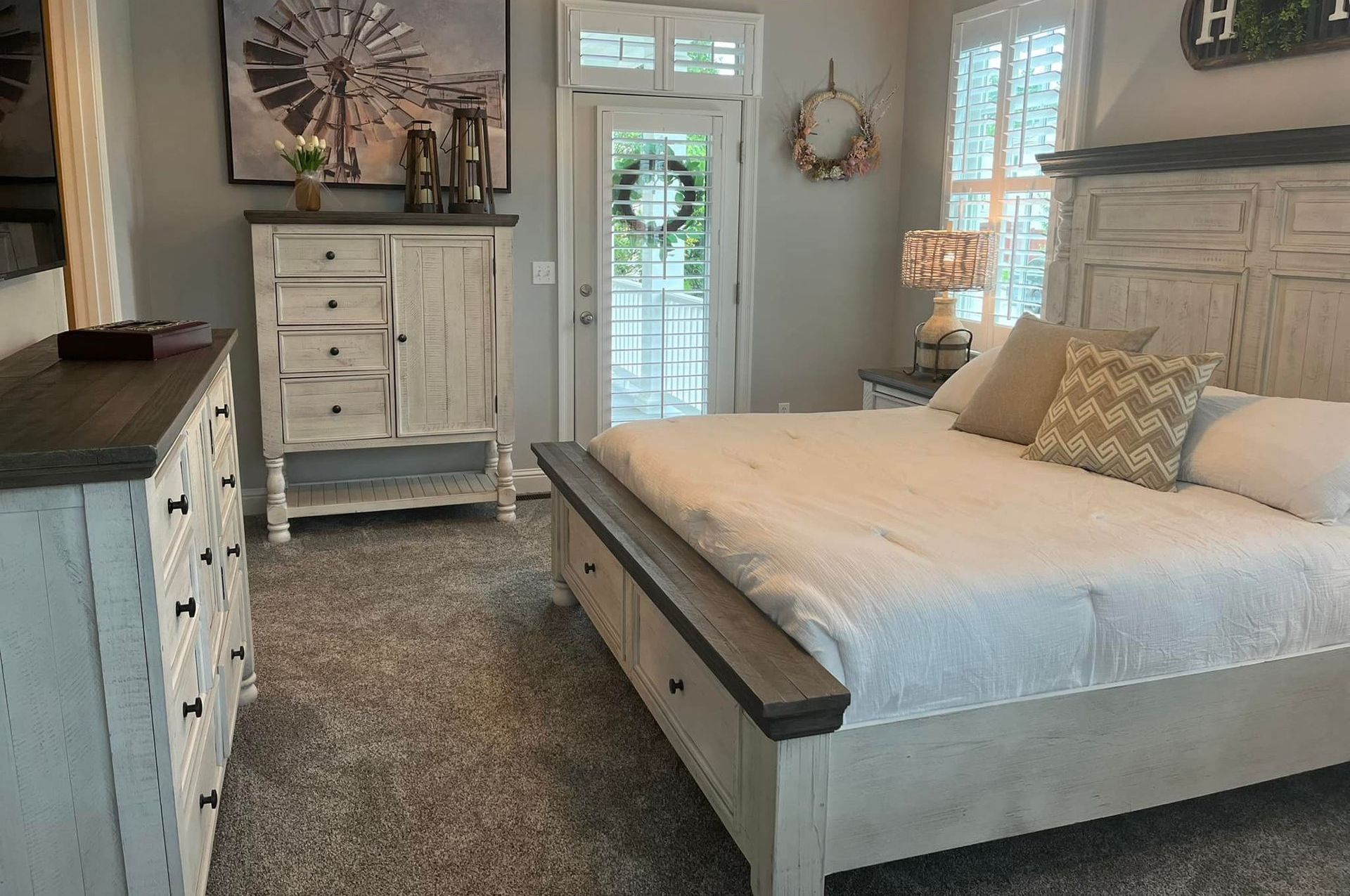 A bedroom with a king size bed , dresser , mirror and shutters.
