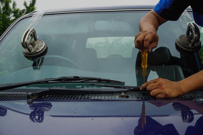 A man is fixing a windshield on a car with a screwdriver.
