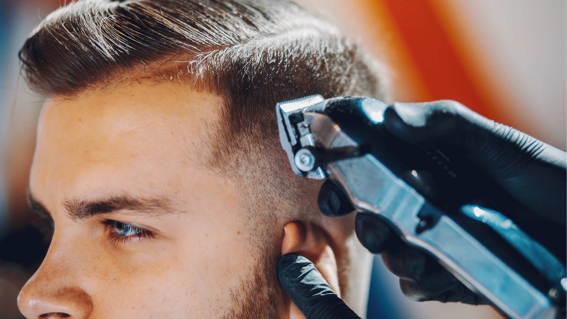 Barber using clippers to cut a client's hair, close-up shot of the ear and sideburn area, indoors.