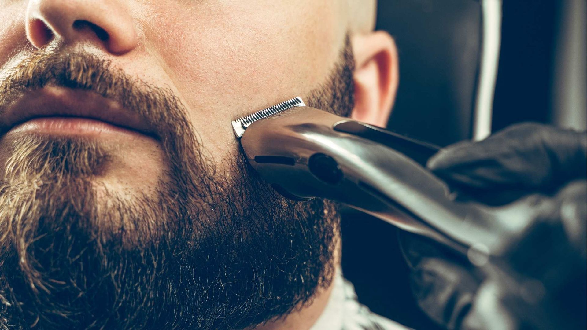 A person's beard being trimmed with an electric razor by a gloved hand; close-up.