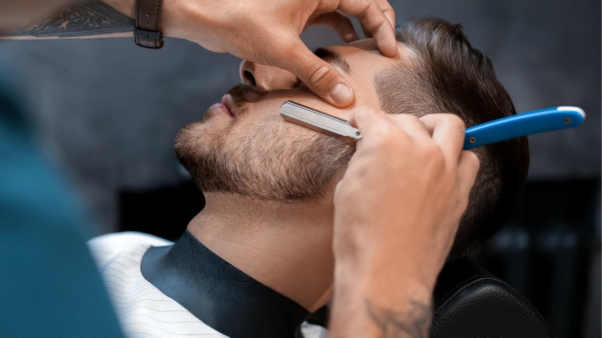 Barber shaves a client's beard with a straight razor in a barbershop.