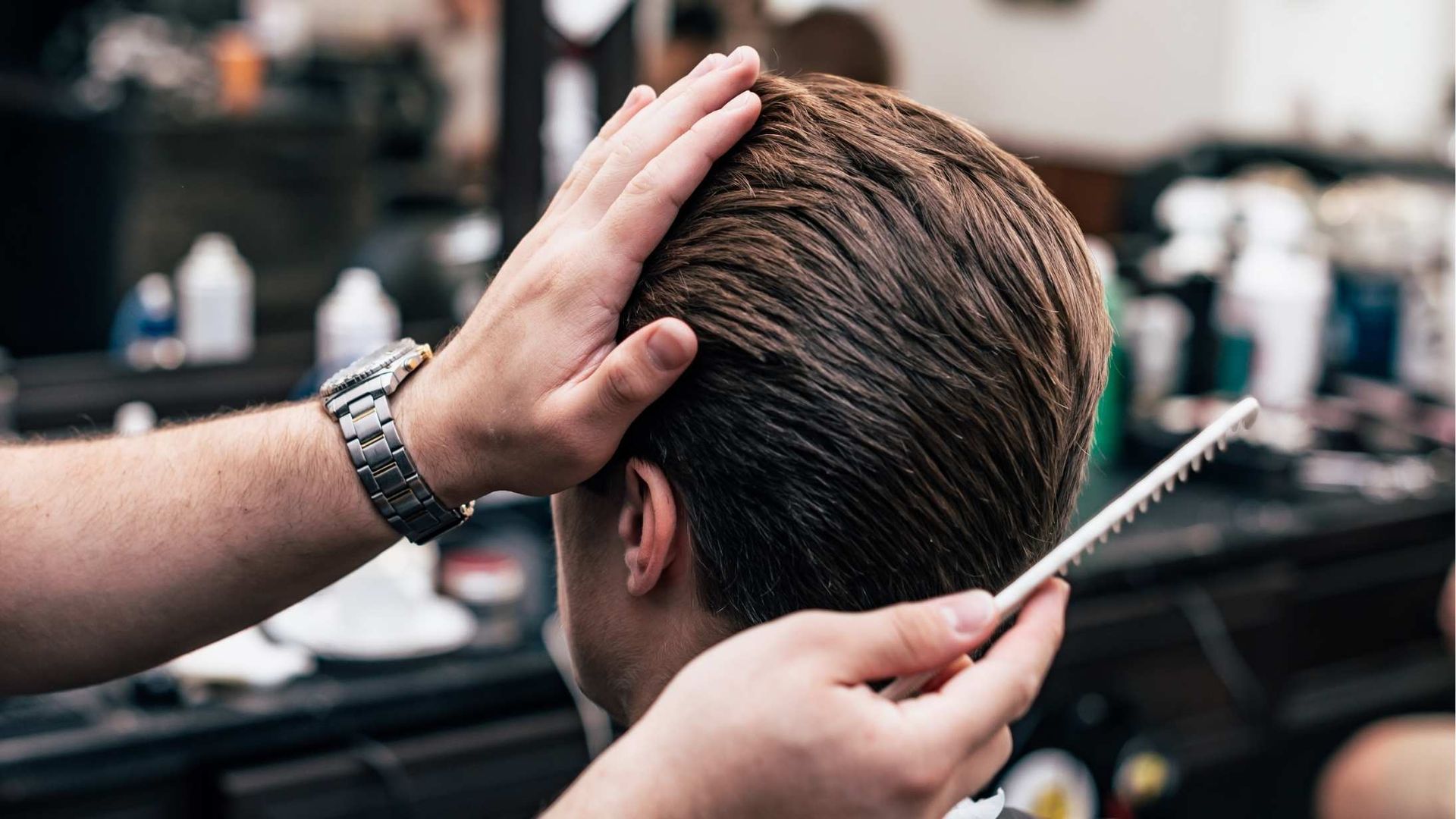Hands combing a person's wet hair in a barber shop. The barber's hand is on the person's head.