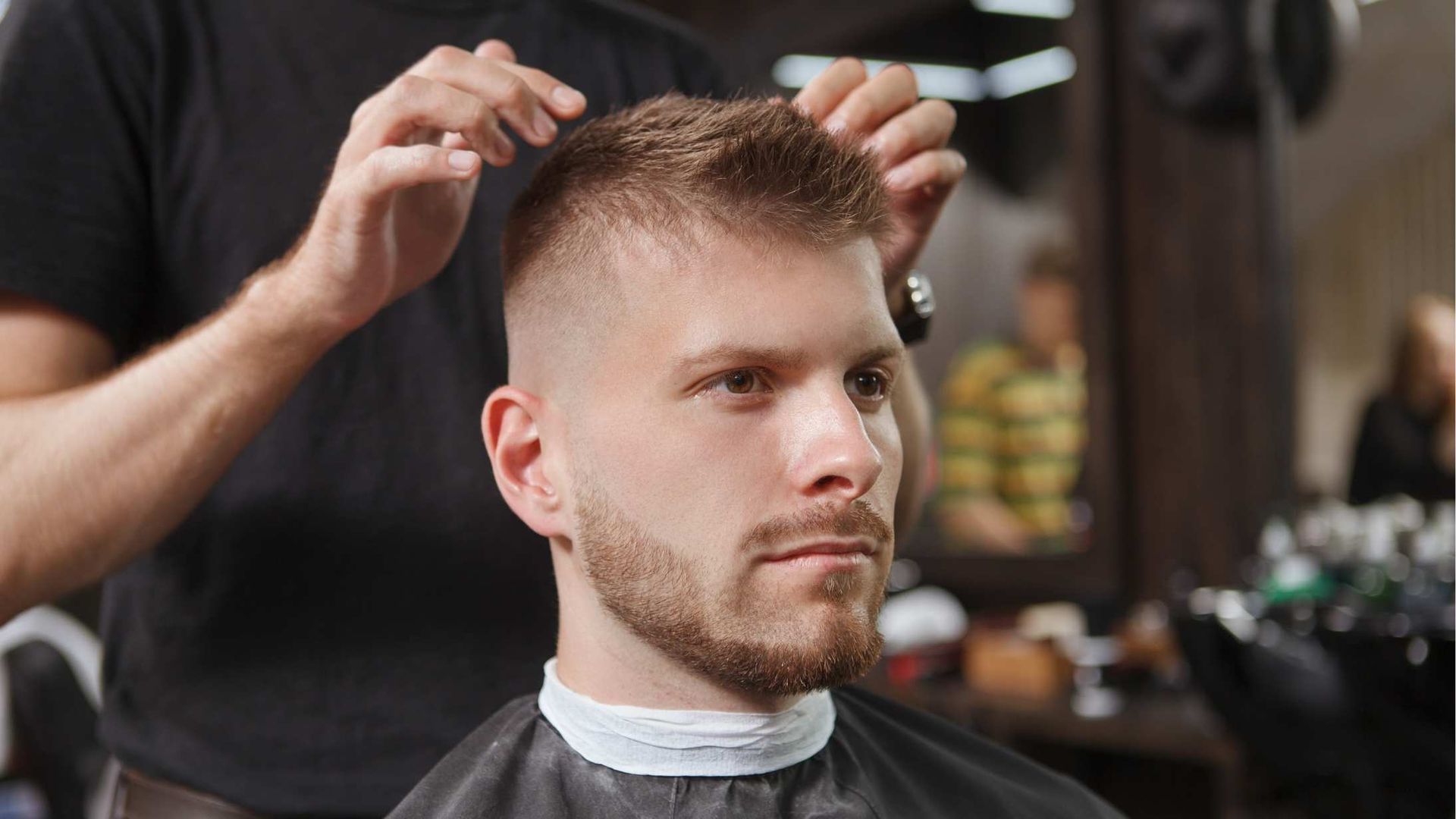 Man getting a haircut at a salon. The barber is styling the man's short, textured hair.