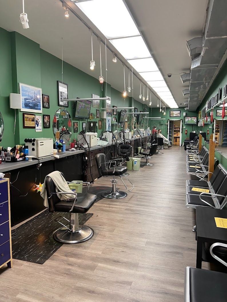 Interior of a barbershop with chairs, mirrors, and tools along a wall. Green walls, bright lighting, and a waiting area.