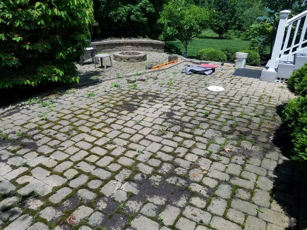 Before image of dirty paved patio requiring, cleaning, repairs and sealing.