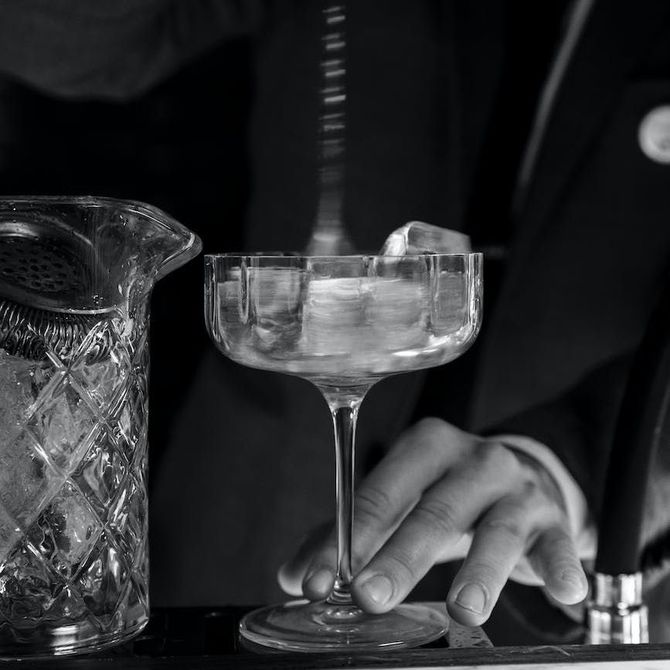 a black and white photo of a bartender pouring ice into a champagne glass