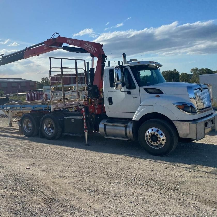 A white truck with a red crane on the back is parked in a dirt lot — White's Truck & Machinery Hire in Bouldercombe, QLD