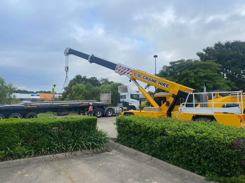 A Large Yellow Crane Is Sitting in A Parking Lot Next to A Truck — White's Truck & Machinery Hire in Bouldercombe, QLD