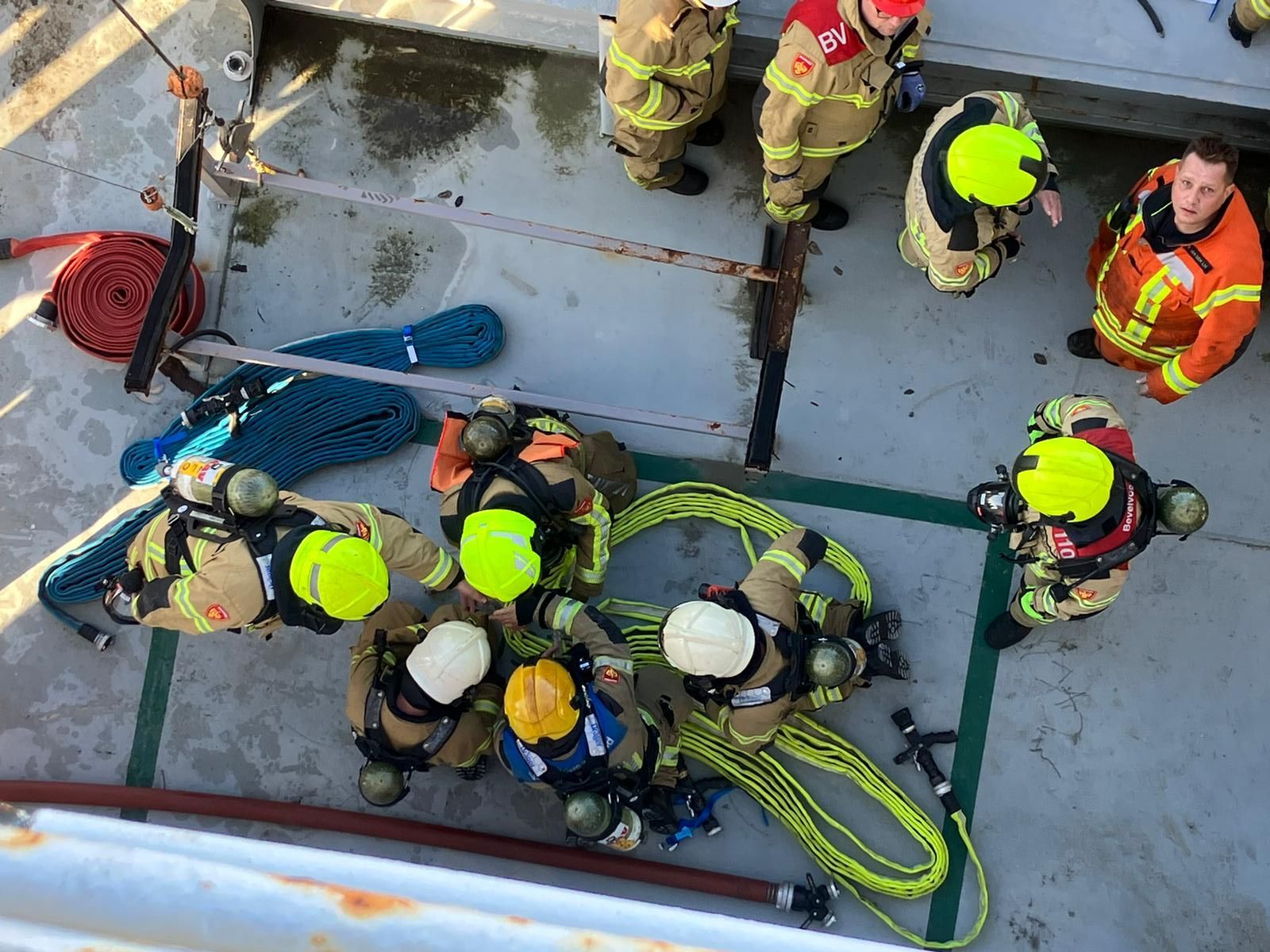 Brandweerlieden in veiligheidsuitrusting oefenen op een bootdek, terwijl ze touwen en uitrusting klaarmaken.