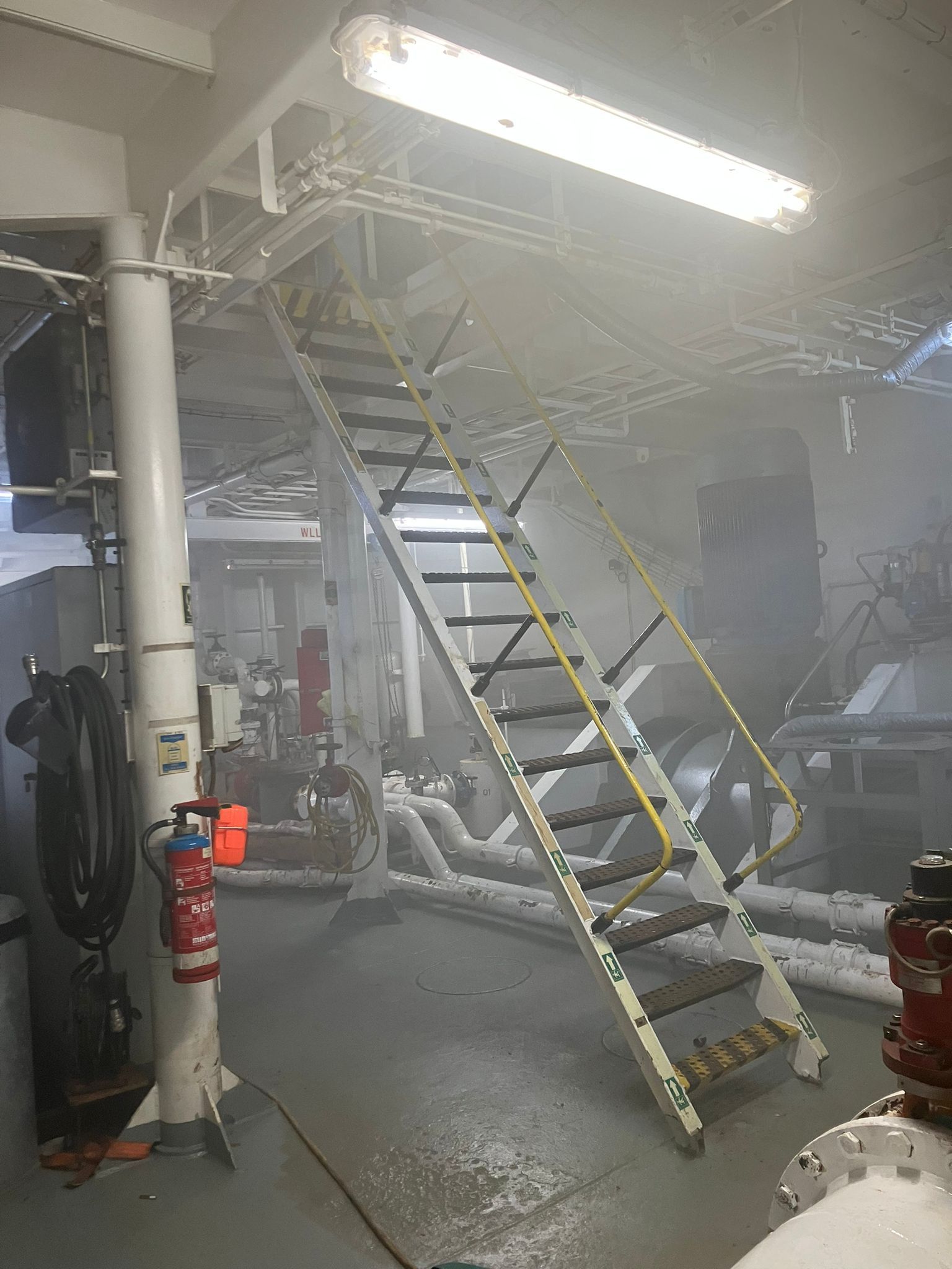 Interieur van een industriële ruimte met trappen, buizen en rook.